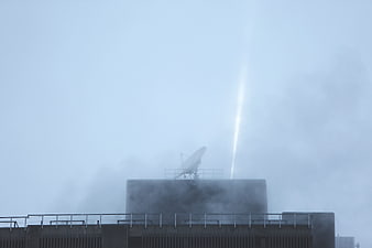 Satellite Dish on Rooftop with Vertical Light Beam in Fog