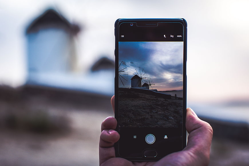 Hand holding smartphone photographing windmills at sunset
