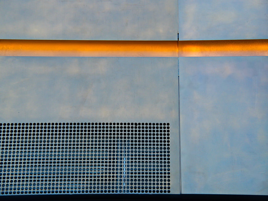 Abstract industrial metal facade with perforated pattern and orange stripe