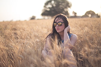Young Woman in Sunglasses Sitting in Golden Wheat Field