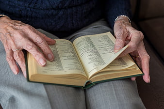 Close-up of elderly hands reading an open book on lap