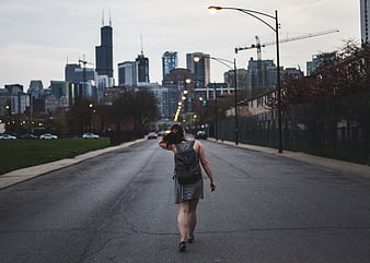 Woman Walking Down City Street with Skyline Background