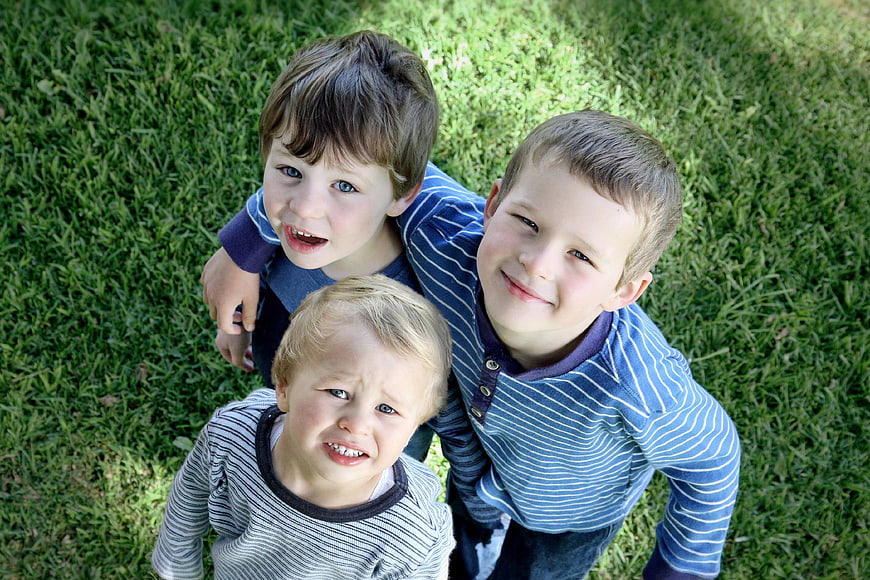 Three young boys looking up from green grass