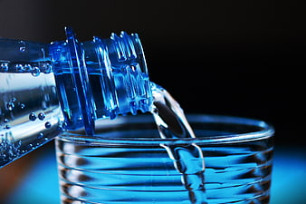 Close-up of water pouring from blue bottle into glass