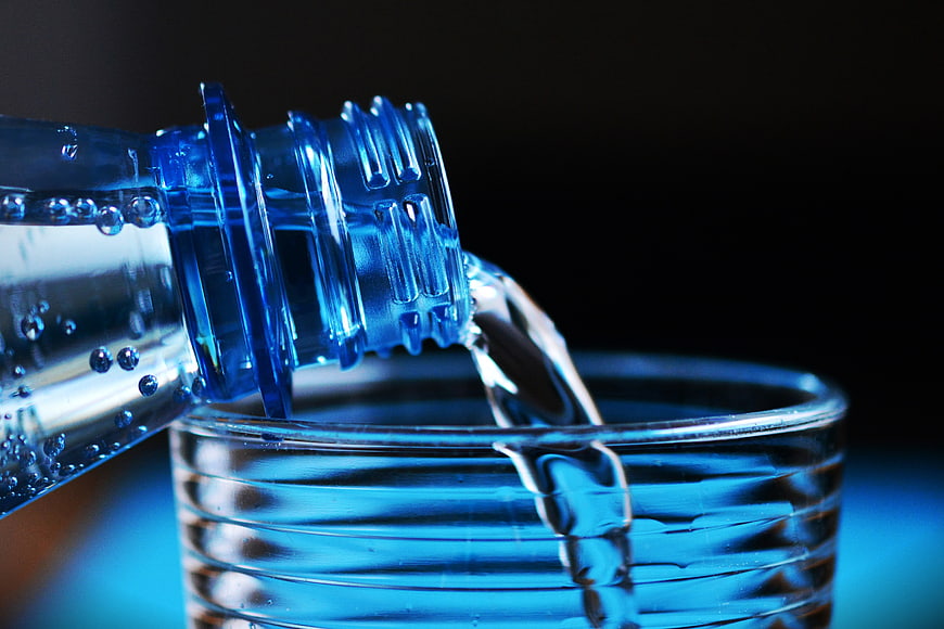 Close-up of water pouring from blue bottle into glass