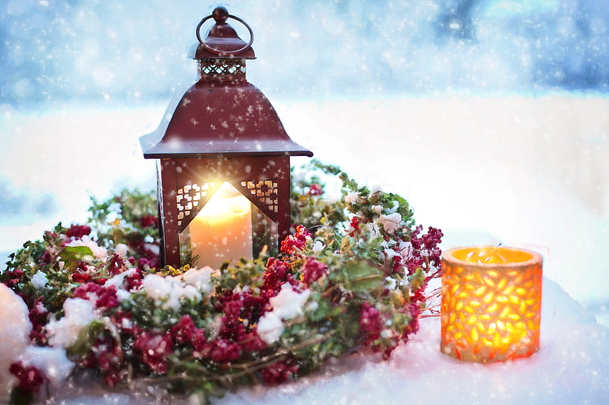 Christmas lantern and candles in snow with festive wreath