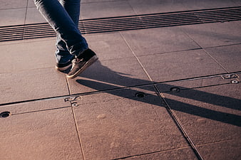 Person Walking on Paved Sidewalk with Long Shadows