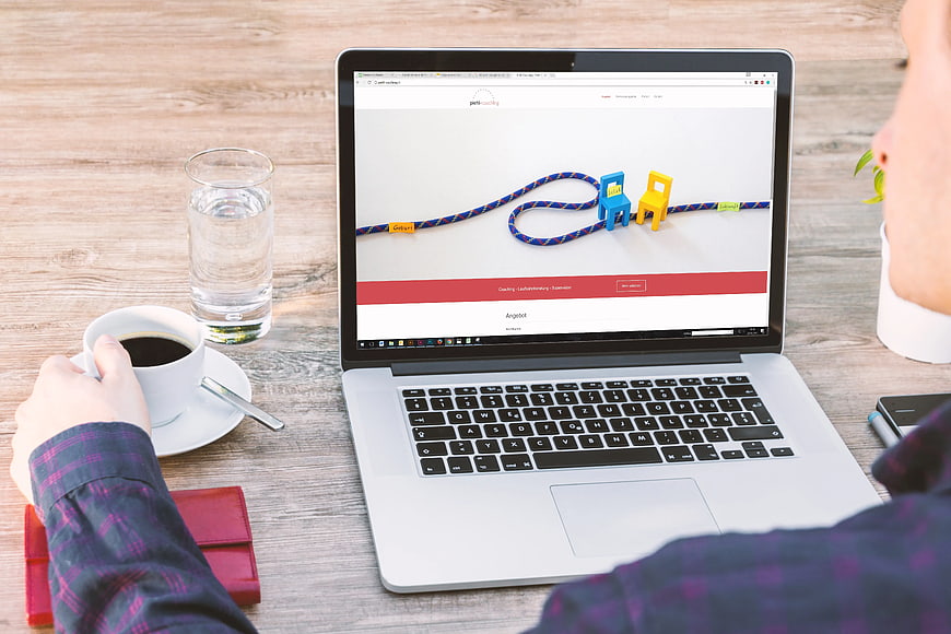 Person browsing coaching website on laptop with coffee