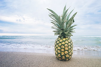 Fresh pineapple on sandy beach with ocean waves background
