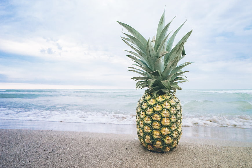 Fresh pineapple on sandy beach with ocean waves background