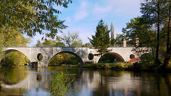 Stone arch bridge over river with autumn trees and reflection