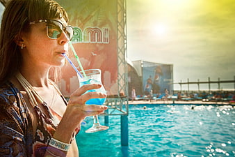 Woman drinking blue cocktail by pool at summer festival