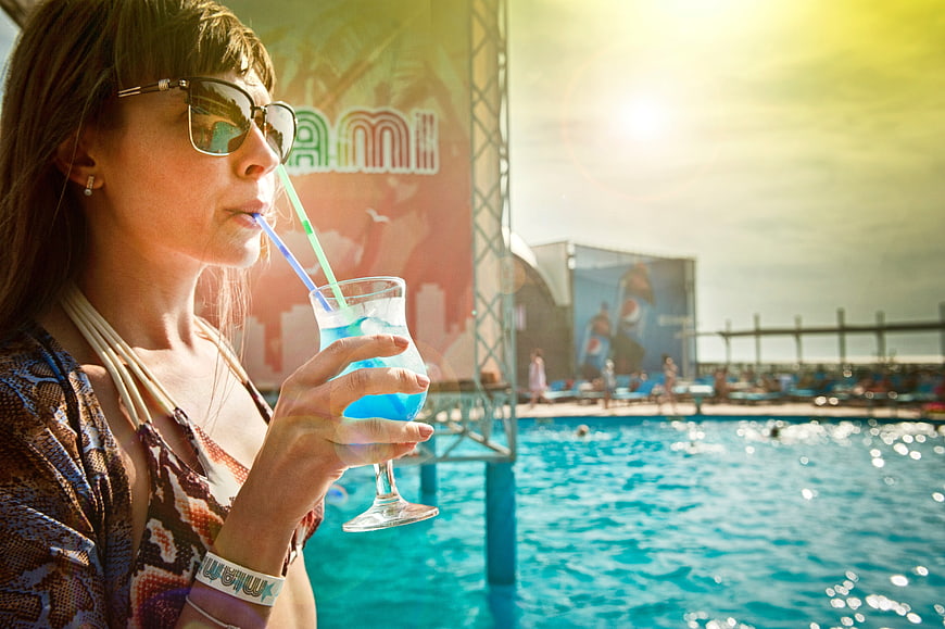 Woman drinking blue cocktail by pool at summer festival