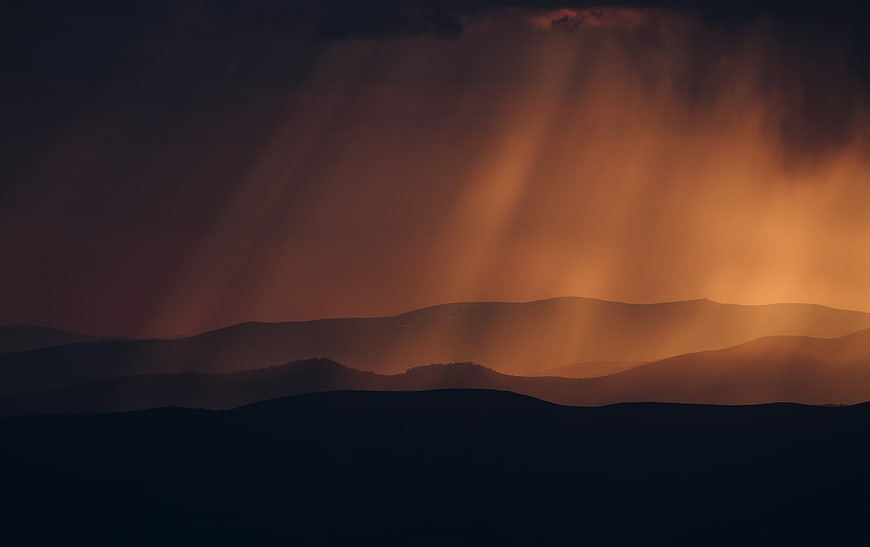 Dramatic sun rays illuminating mountain silhouettes at dusk