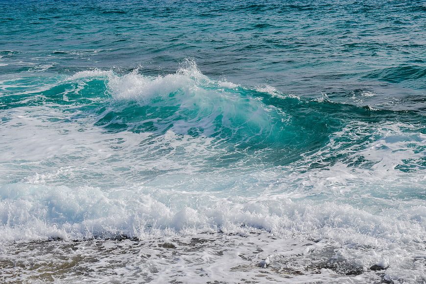 Turquoise ocean wave crashing with white foam on beach