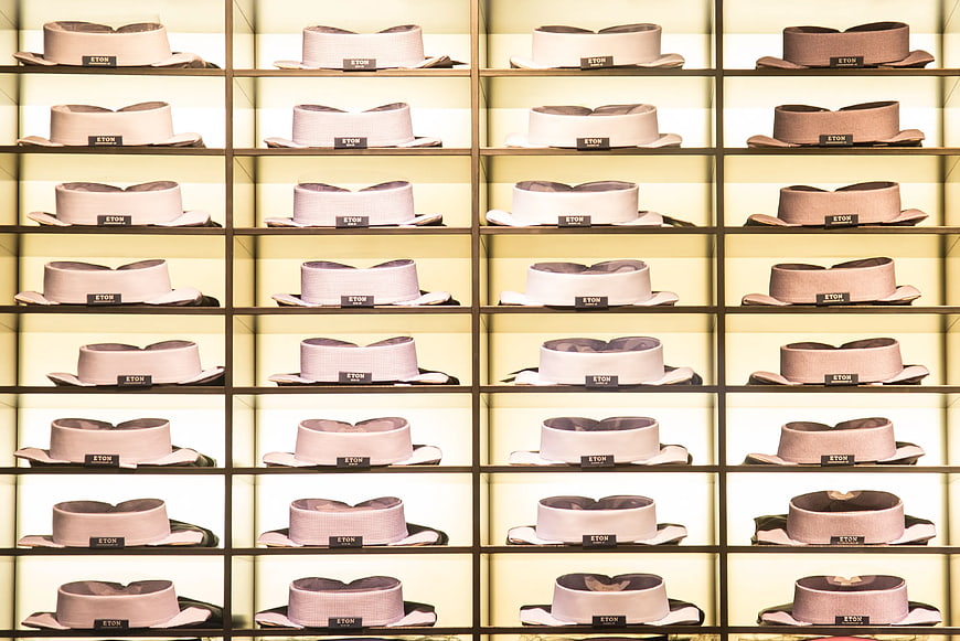 Grid of beige and brown fedora hats on illuminated shelves