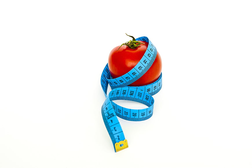 Red Tomato Wrapped in Blue Measuring Tape on White Background