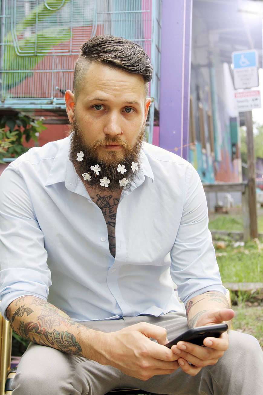 Tattooed Man with Flowers in Beard Using Smartphone