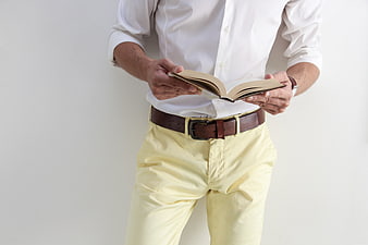 Man in white shirt and yellow trousers reading a book