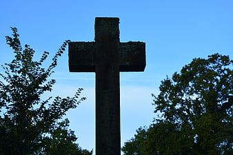 Silhouette of weathered stone cross against blue sky