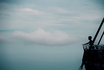 Silhouette of Man Looking at Clouds from High Platform
