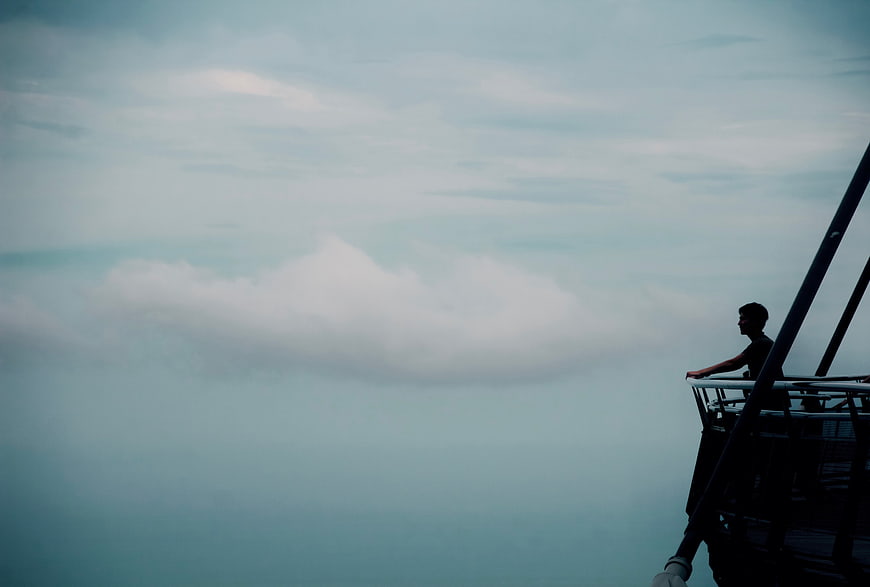 Silhouette of Man Looking at Clouds from High Platform