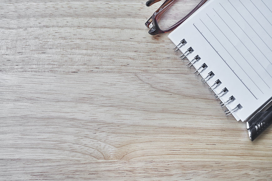 Minimalist workspace with notebook, pen, and glasses on wood