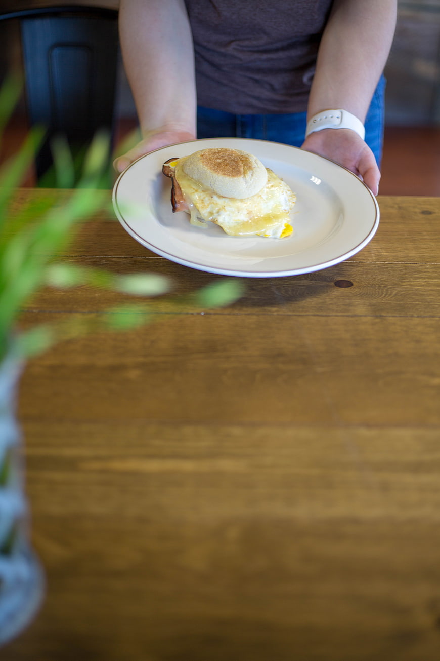 Person serving breakfast sandwich on wooden table