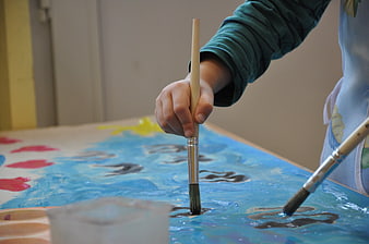 Child's hand holding paintbrush applying blue paint on canvas