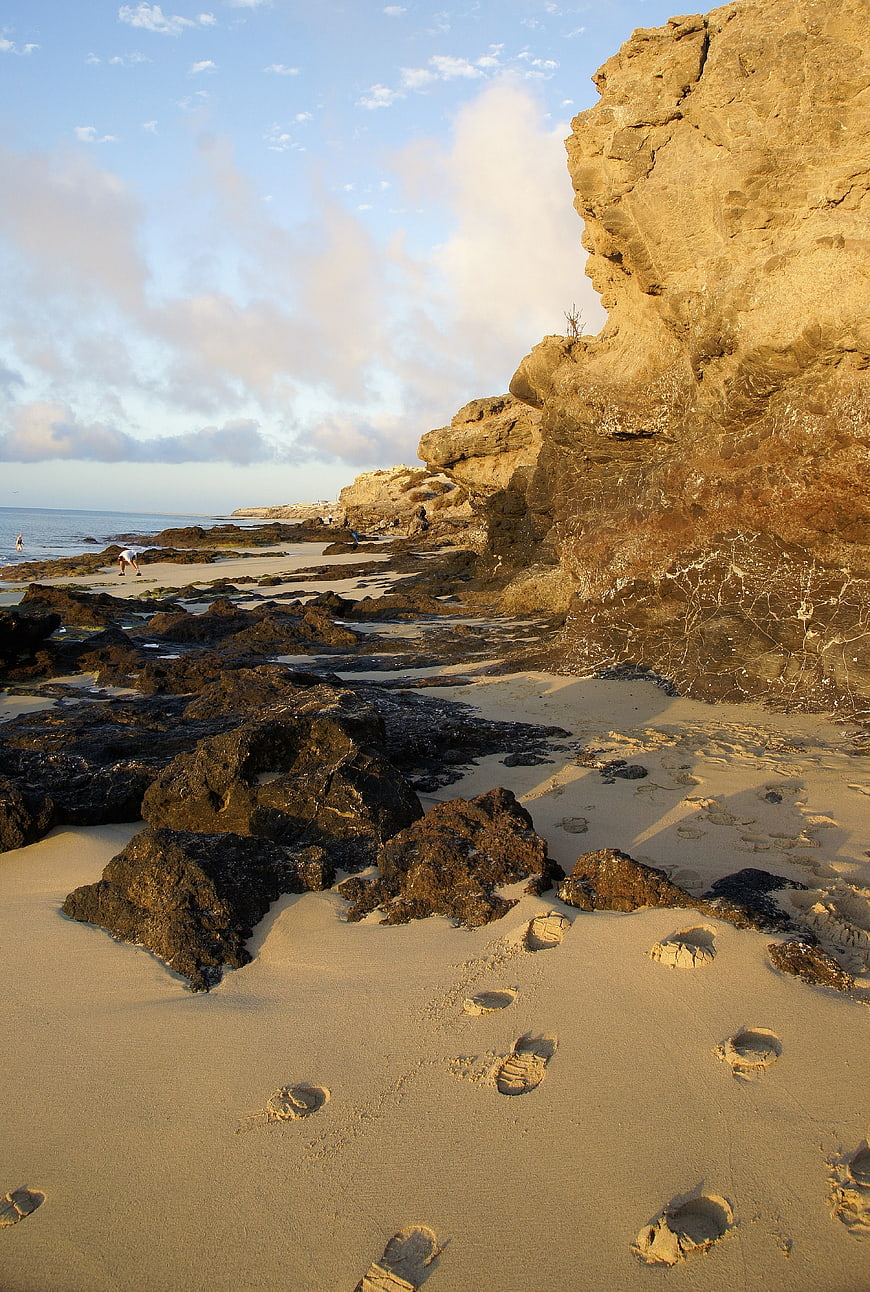 Footprints in sand on rocky beach at sunrise