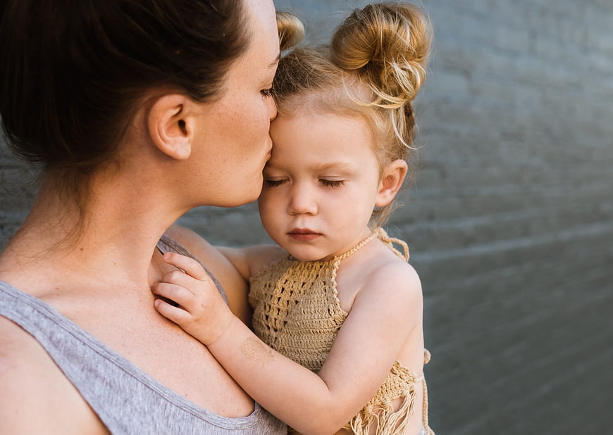 Mother kissing daughter's forehead in tender outdoor portrait