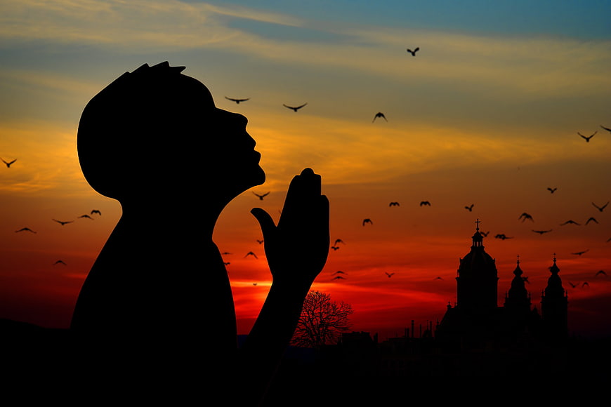 Silhouette of man praying at sunset with church and birds