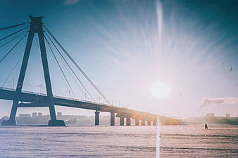 Silhouette of cable-stayed bridge over frozen river at sunrise