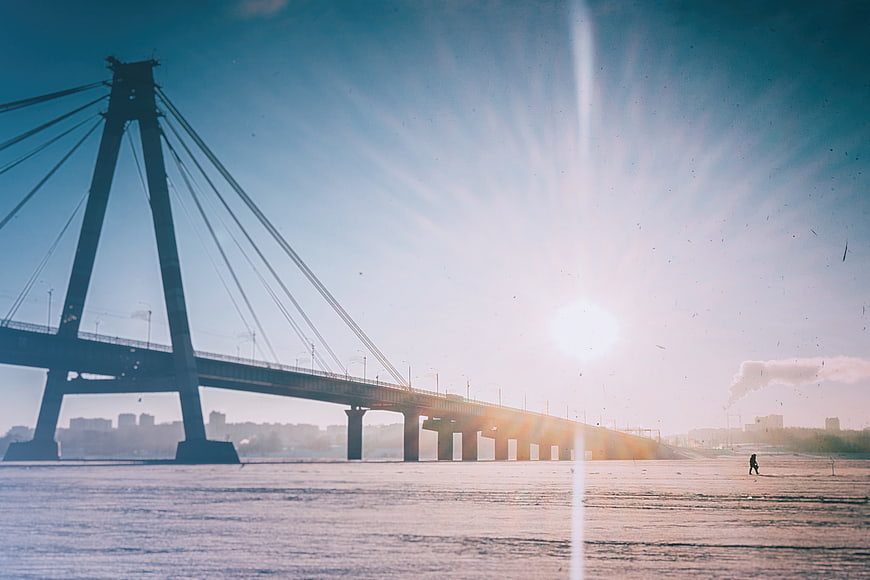 Silhouette of cable-stayed bridge over frozen river at sunrise