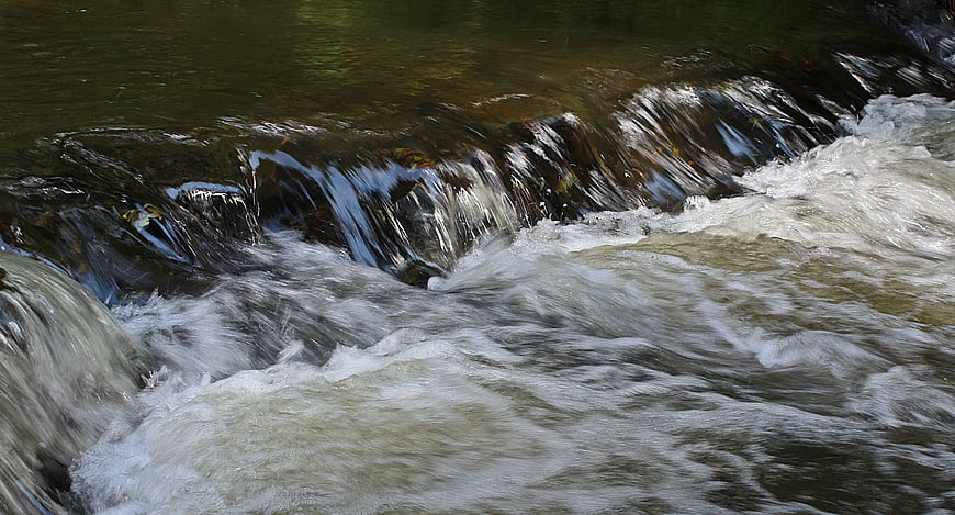Flowing River Water Over Rocks with White Foam