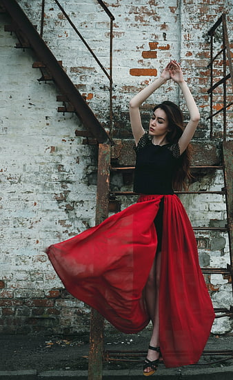 Young Woman in Black Top and Flowing Red Skirt Against Weathered Brick Wall
