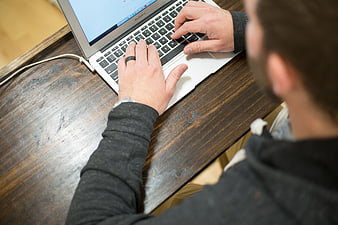 Man Typing on Laptop at Wooden Desk