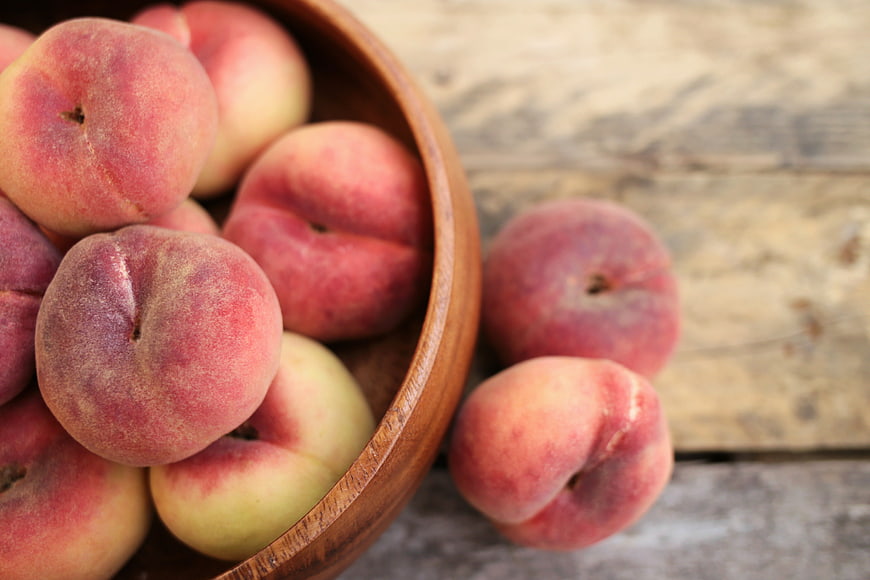 Fresh ripe peaches in a wooden bowl on rustic table