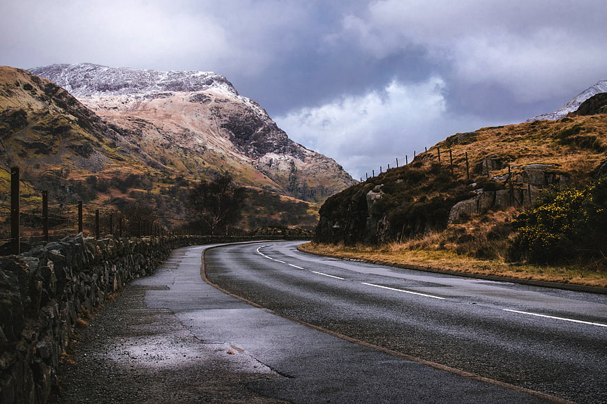 Winding Mountain Road with Snow-Capped Peaks and Dramatic Clouds
