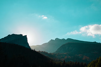 Dramatic Mountain Silhouette with Sun Flare and Blue Sky