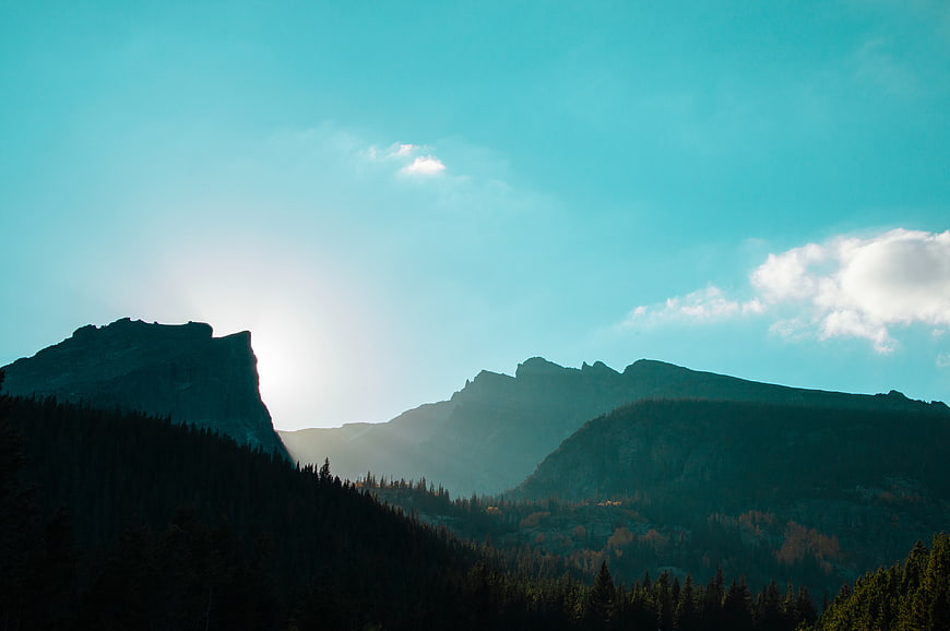 Dramatic Mountain Silhouette with Sun Flare and Blue Sky