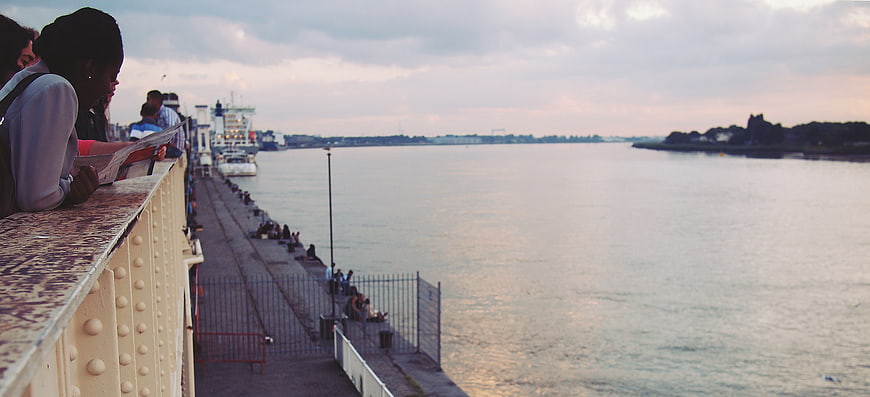 People leaning on bridge railing overlooking river at dusk