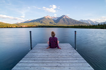 Woman Sitting on Wooden Dock Facing Serene Lake and Mountains