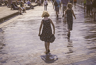 Two young girls walking away on wet pavement
