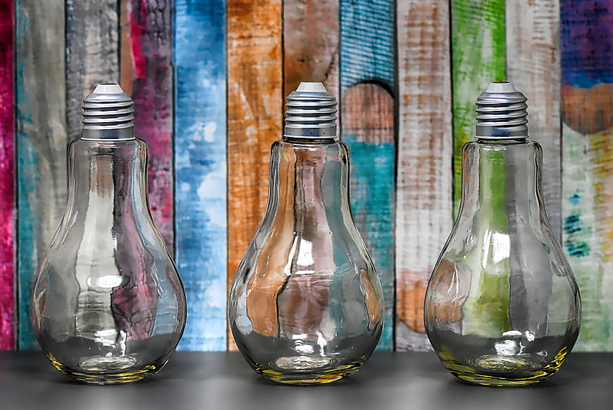 Three empty glass lightbulbs on a dark surface against a colorful painted wooden background