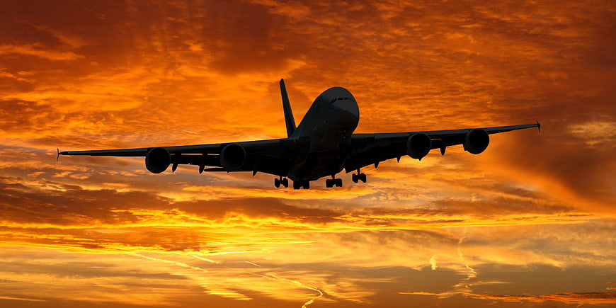 Silhouette of Large Airplane Landing Against Vibrant Orange Sunset Sky