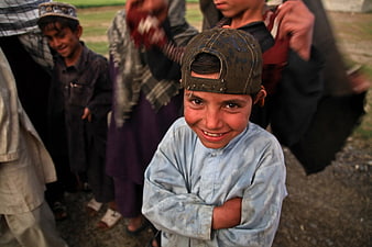 Smiling Afghan boy wearing a worn cap in a rural village setting