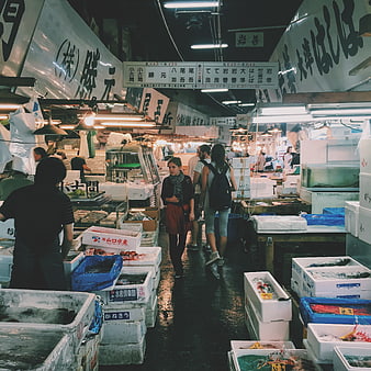 Tourists walking through a busy Japanese fish market aisle