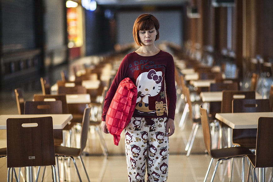 Woman in pajamas holding pillow in empty dining hall