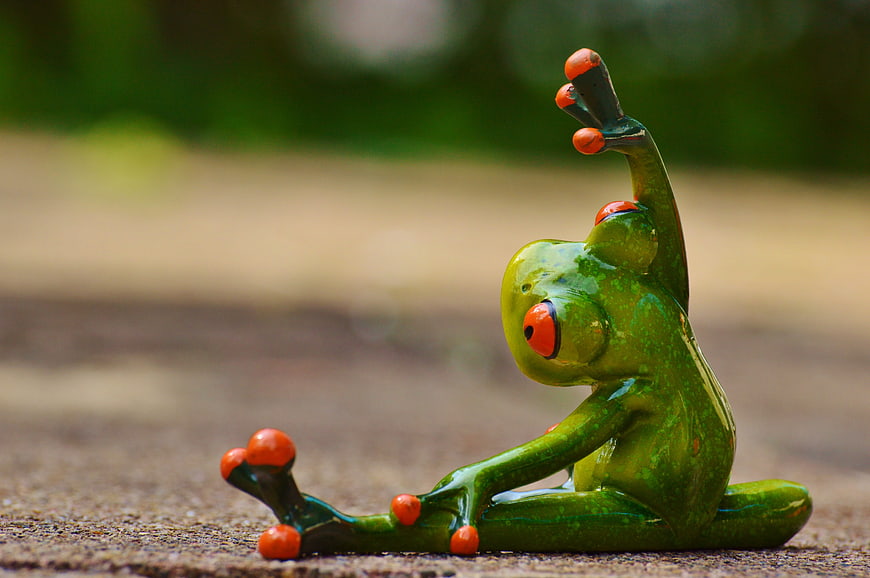 Green ceramic frog figurine doing yoga pose on stone